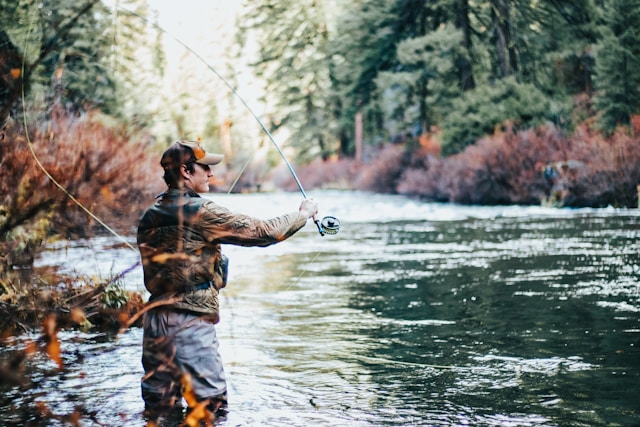A man fishing in a river with a fly rod, enjoying the tranquility of nature and the thrill of angling.